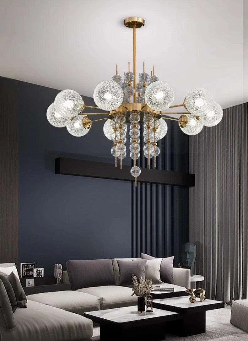 Modern chandelier hanging in a living room with a gray sofa and dark walls.