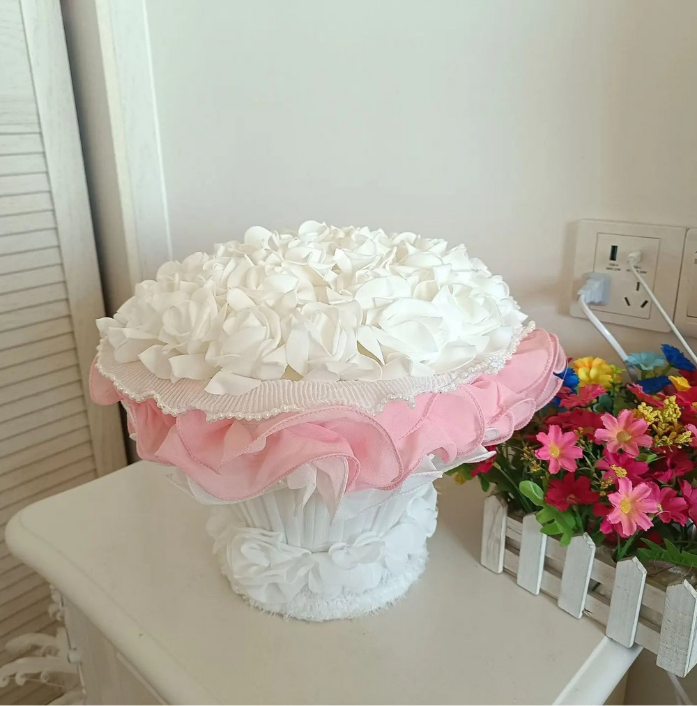 Decorative white flower arrangement in a pink and white vase on a table.