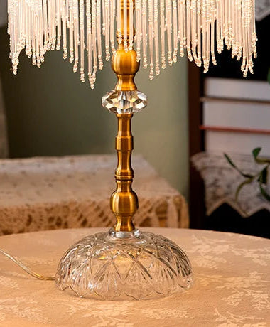 Decorative lamp with crystal base and gold accents on a table with floral arrangements.