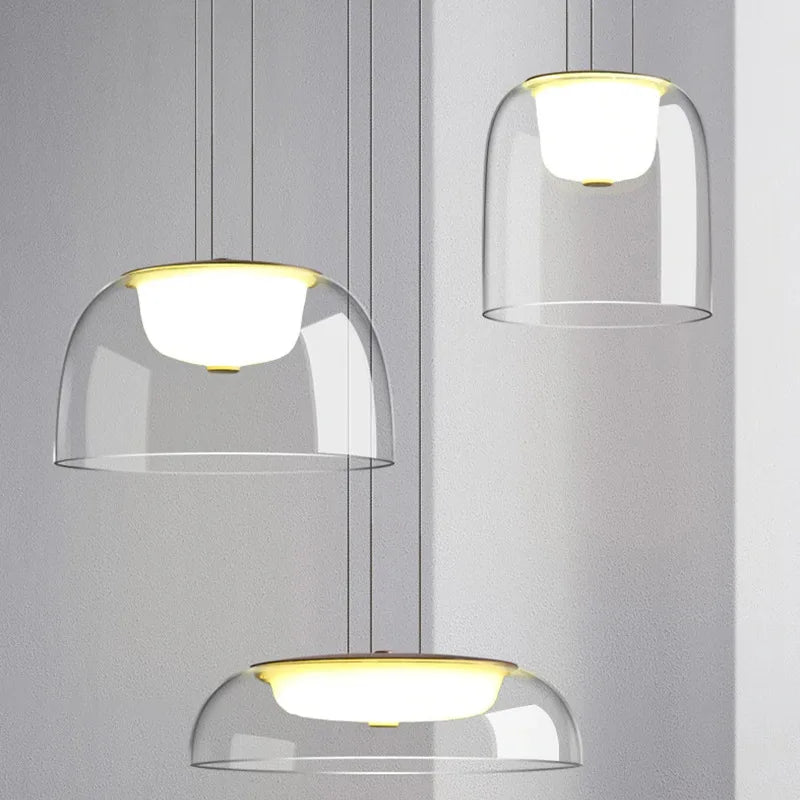 Three clear glass dome pendant lights with gold accents hanging against a light gray background.