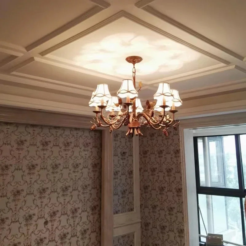 Close-up view of a gold chandelier with fabric shades and detailed bird figures, mounted on a coffered ceiling.