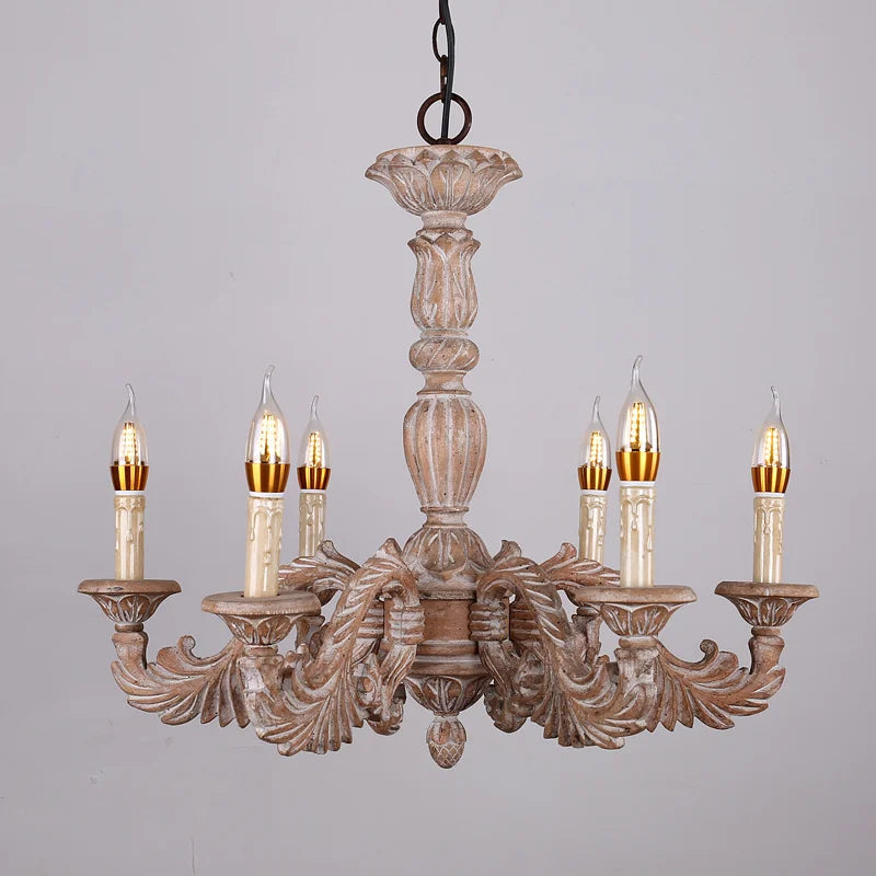 Close-up of a distressed wood chandelier with candelabra-style arms, intricate carvings, and detailed floral accents against a white background.