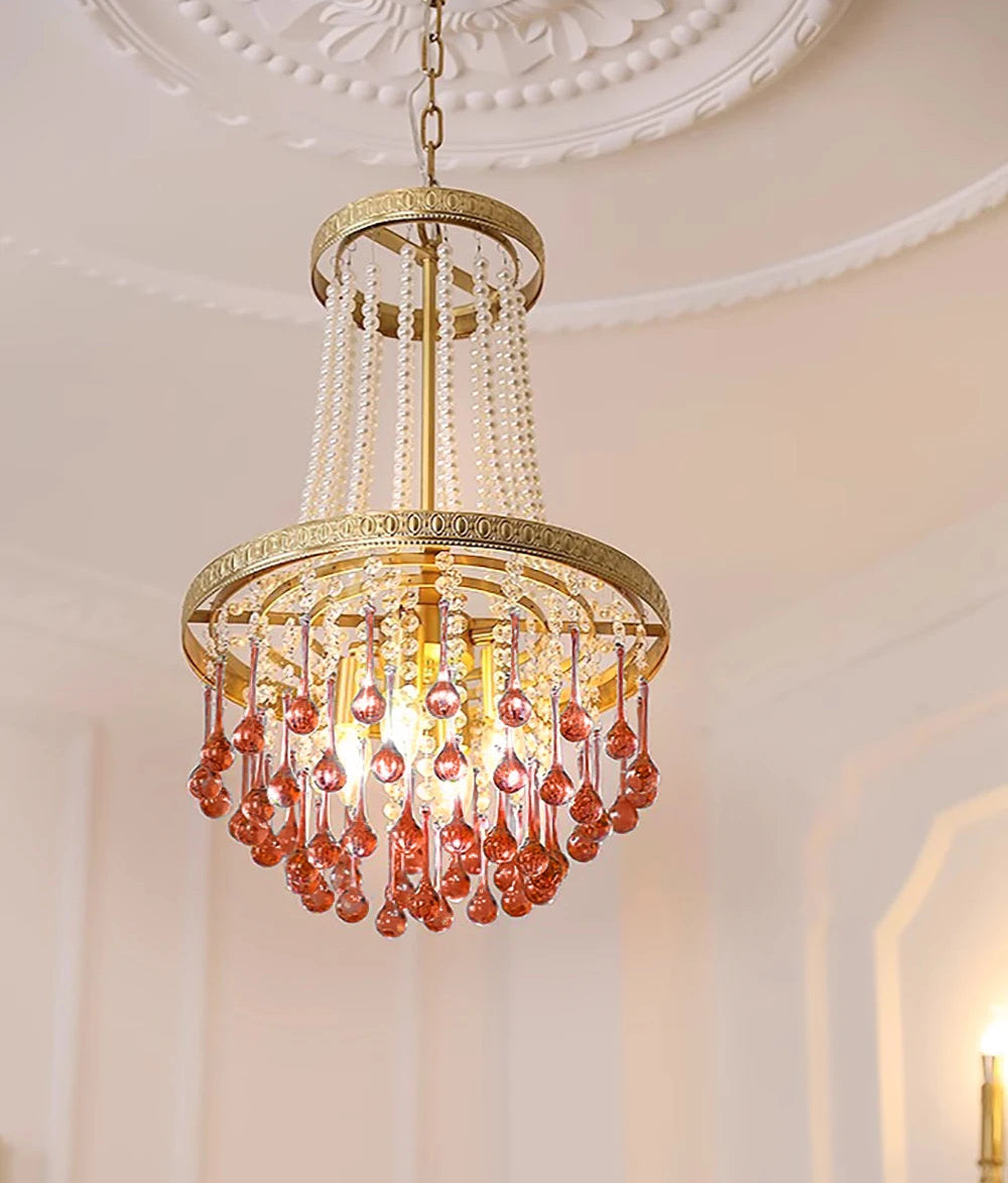 Gold chandelier with red crystal accents hanging in a room with white walls and a ceiling light fixture.