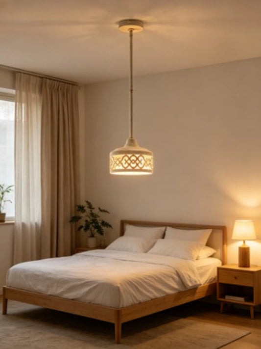 A bedroom with a white drum pendant light featuring gold scrollwork hanging above a wooden bed frame.