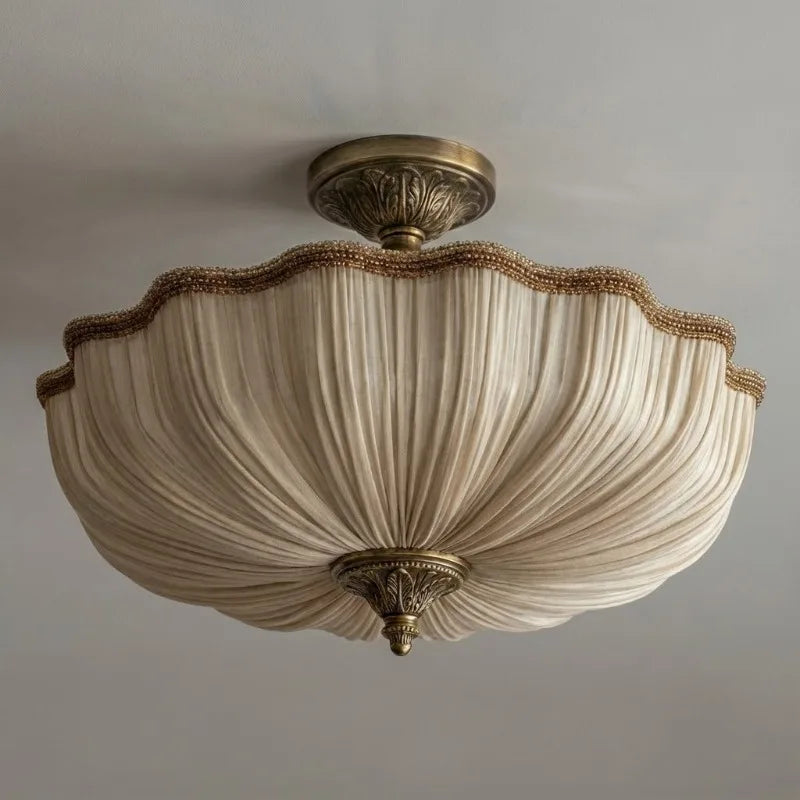 A beige fabric pleated semi-flush ceiling light with ornate gold-toned hardware, shown from a slightly different angle