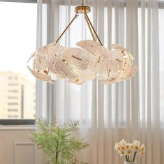 The gold woven floral pendant light illuminated in a room setting with sheer curtains in the background.