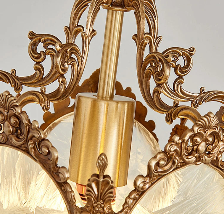 Decorative gold light fixture with intricate designs on a gray background.