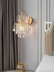 Gold wall sconce with pink and clear crystals, next to a draped curtain and a bedside table.