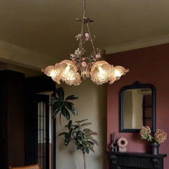 Close-up of a gold chandelier with intricate floral rose bud details and textured glass shades, illuminated in a dimly lit room.