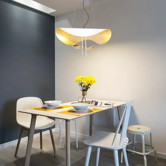 A dining room setting featuring a white and gold leaf wave pendant light above a table.