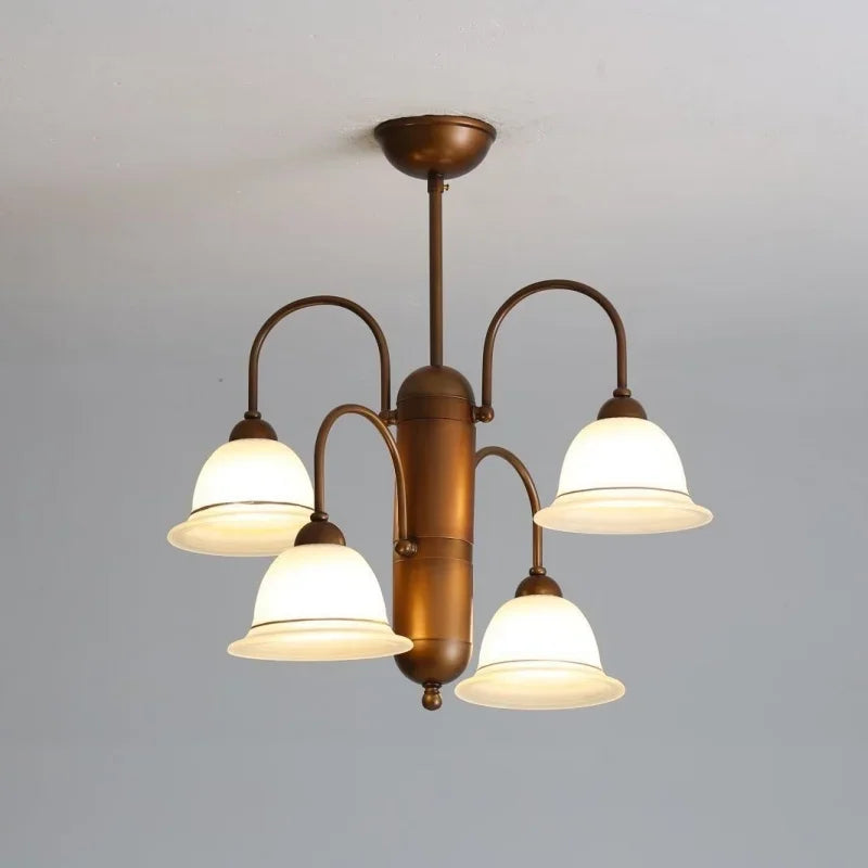 A close-up, low-angle shot of a brushed gold chandelier with four frosted glass bell-shaped shades arranged symmetrically on curved arms, mounted on a white ceiling.