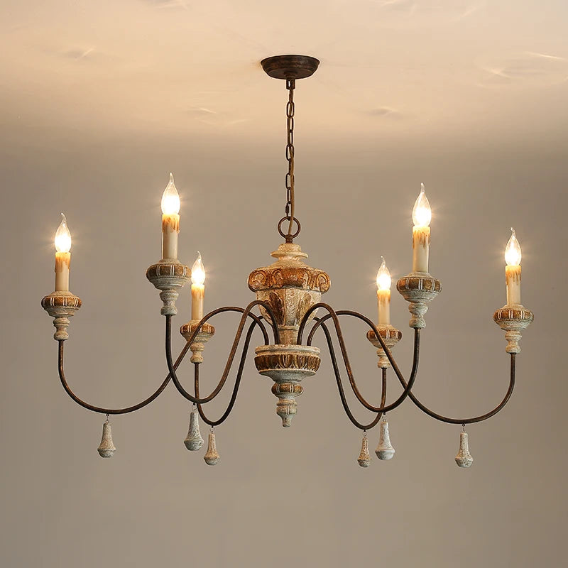 A distressed wood and iron chandelier with six candle-style lights against a plain background.