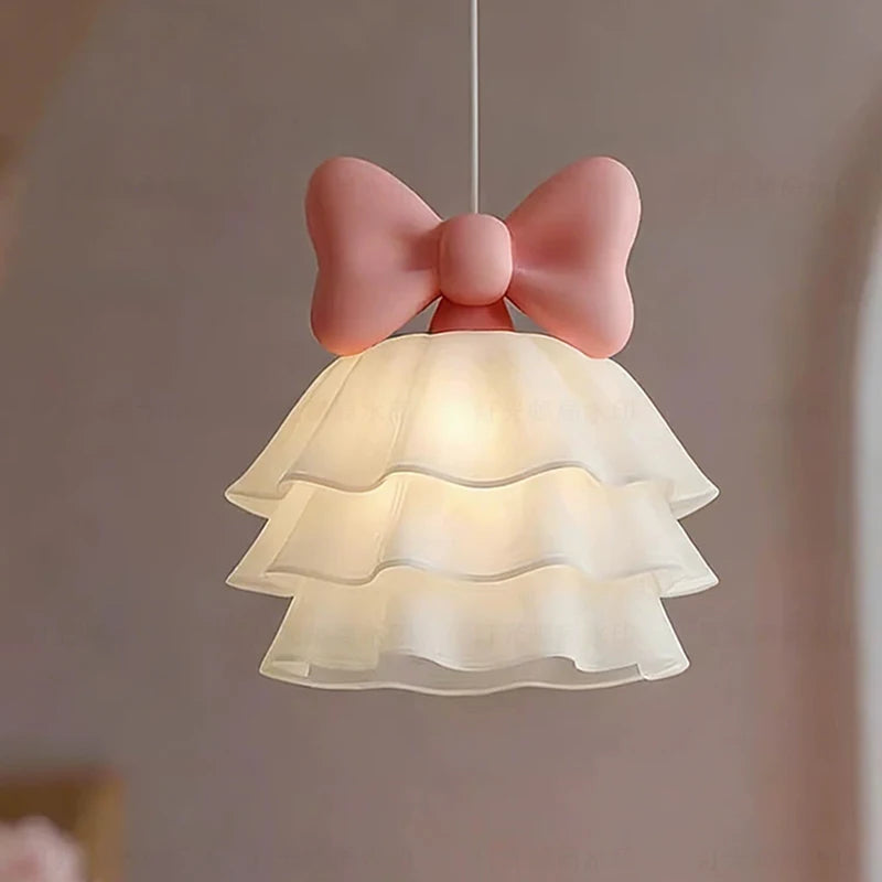 Close-up of a white tiered shade with a pink bow on top, lit from within.