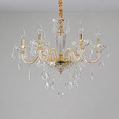 A gold crystal chandelier with multiple arms and dangling crystals, shown in a close-up view against a light gray wall.