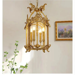 A gold candelabra cage pendant light viewed from a slightly lower angle, with a plant in the foreground.