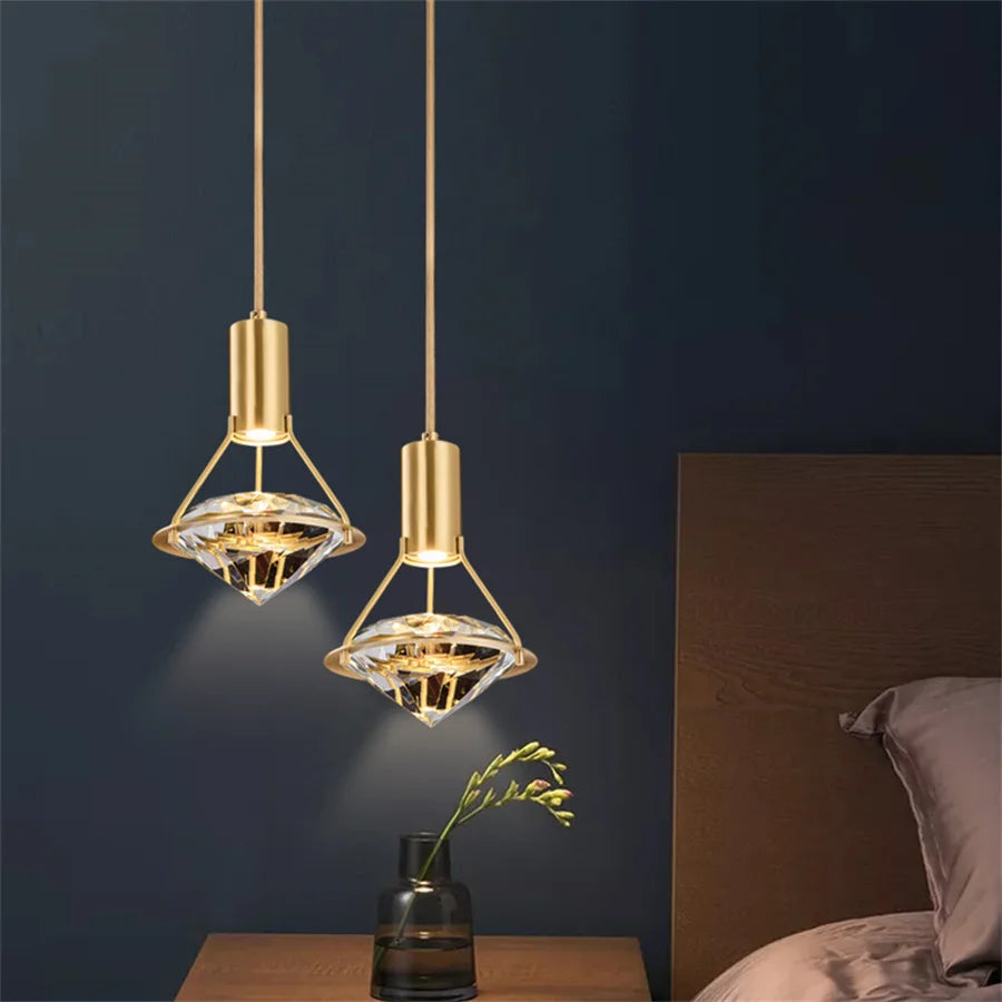 Two gold pendant lights hanging against a dark wall with a vase and plant on a table.