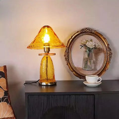 A textured amber glass mushroom-shaped table lamp with a metal base sits on a dark wooden cabinet.