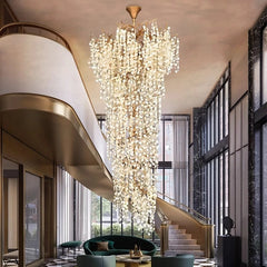 An expansive gold-framed crystal chandelier cascades in a luxurious foyer with a checkered marble floor and a curved staircase.