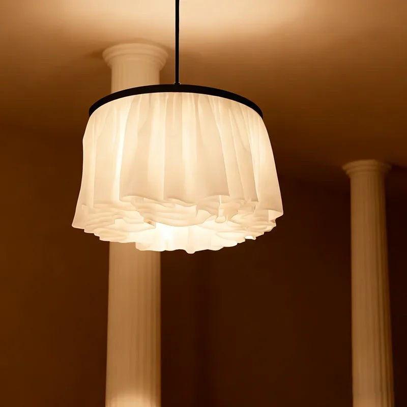 A white fabric ruffled pendant light suspended from the ceiling, with architectural columns in the background.