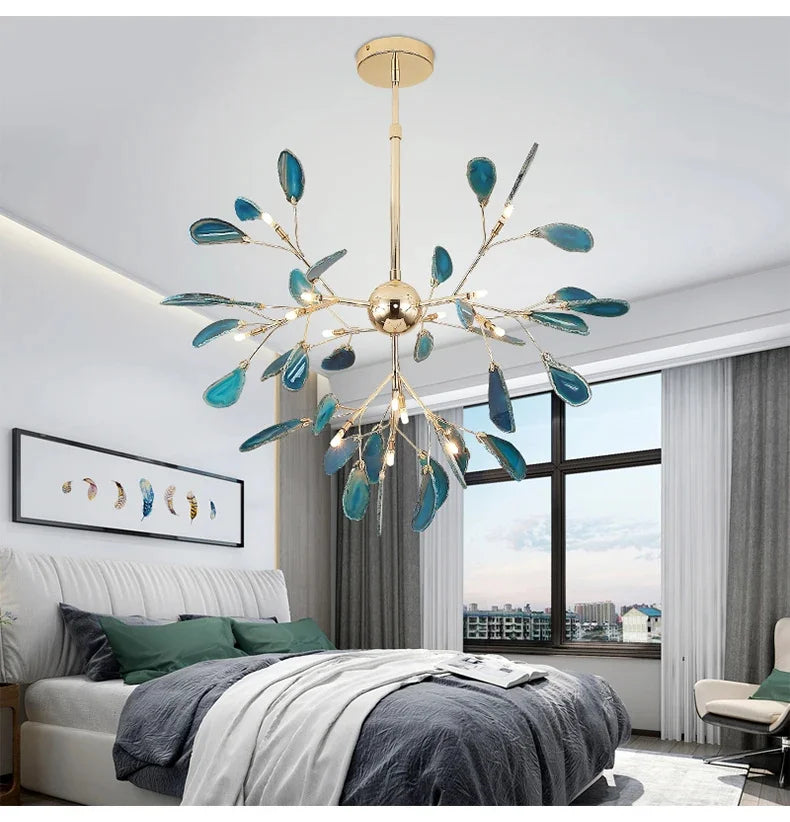 Gold leaf-shaped chandelier with blue accents hanging in a bedroom with white walls and large window.