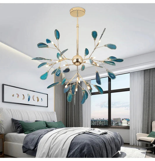 Gold leaf-shaped chandelier with blue accents hanging in a bedroom with white walls and large window.