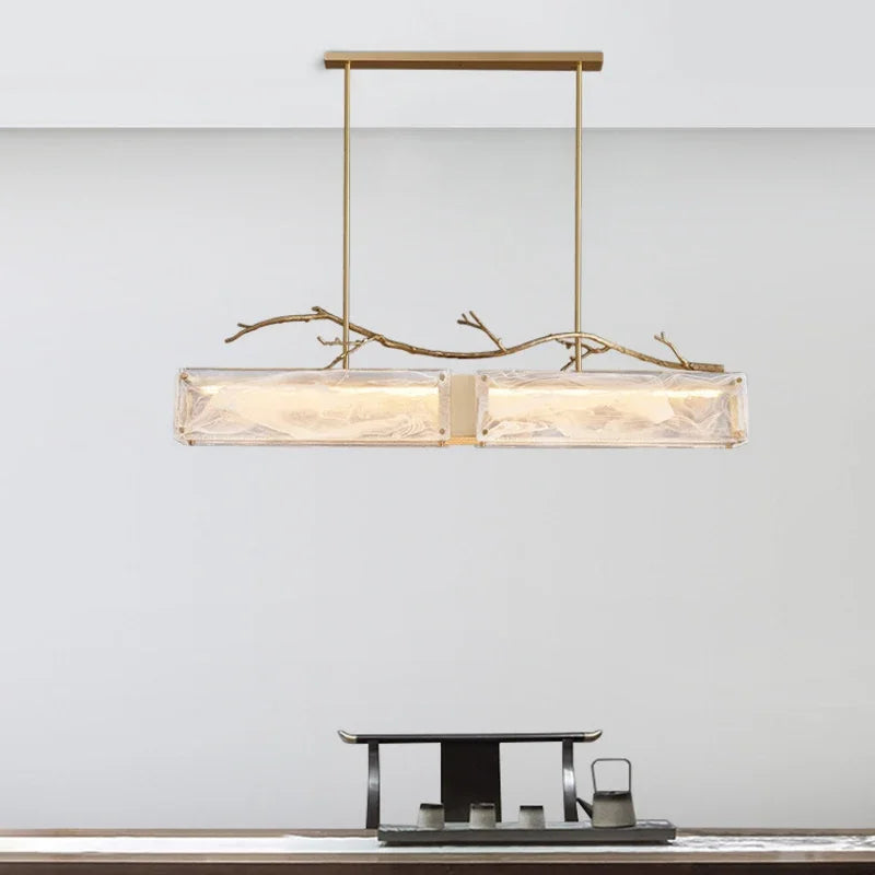 Rectangular glass pendant light with brushed gold branch accents against a plain background.