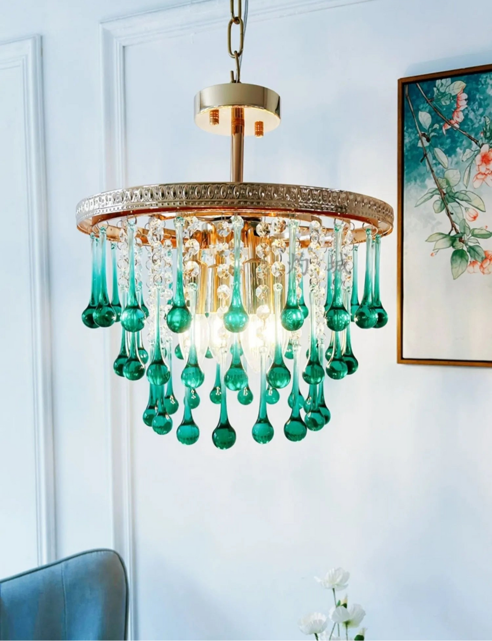 Chandelier with green crystal droplets in a room with a painting on the wall.