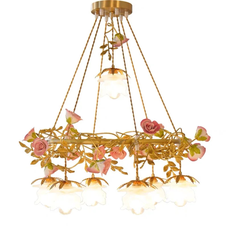 Frontal view of a gold pendant light featuring a ring structure with intertwined ceramic pink roses and green leaves, suspended by golden cords.