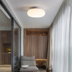 White flush mount ceiling light above a chair and wooden cabinets