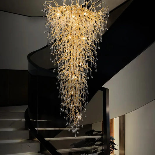 A grand gold cascading chandelier with crystal teardrops illuminating a modern staircase.