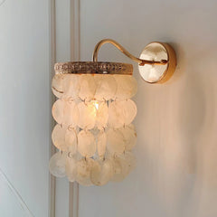 Close-up of a gold wall sconce with white shell accents, showcasing the textured metal rim and mounting plate.
