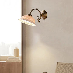 A gold and white ceramic floral wall sconce mounted on a textured wall, with soft lighting casting shadows.