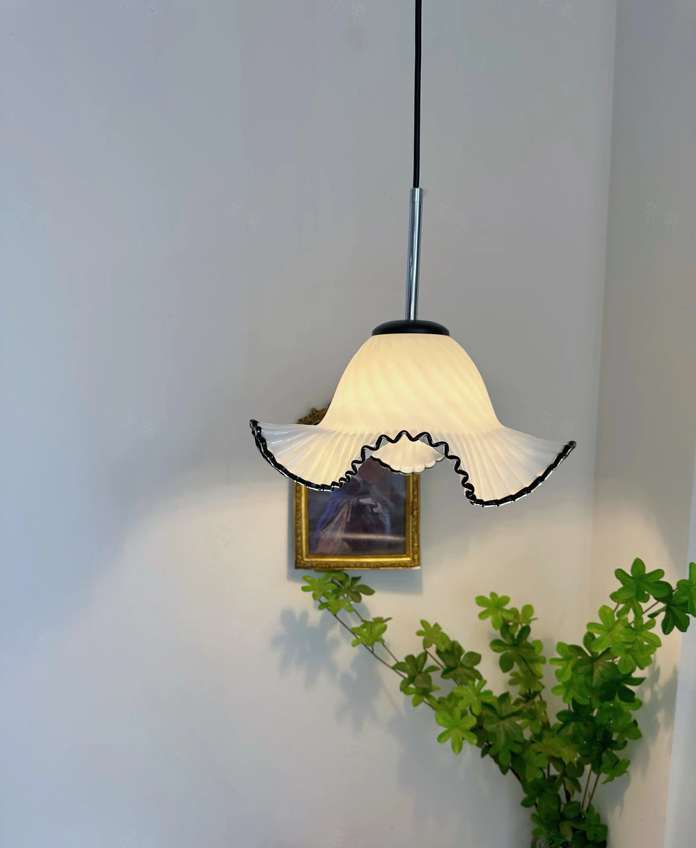 A white glass fluted pendant light with black trim hangs in a brightly lit room, with a painting and greenery visible.