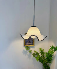 A white glass fluted pendant light with black trim hangs in a brightly lit room, with a painting and greenery visible.