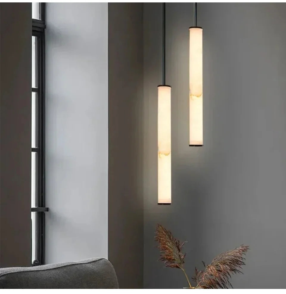Two marble cylinder pendant lights with natural stone veins hanging in a modern interior space.