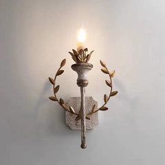 Distressed gold metal wall sconce with a leaf wreath design and a single candle-style light, mounted on a light blue wall.