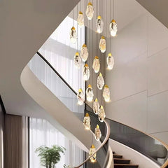 Interior shot of a stylish staircase and foyer, highlighted by the dramatic descent of a multi-tiered gold chandelier adorned with sparkling faceted crystals.
