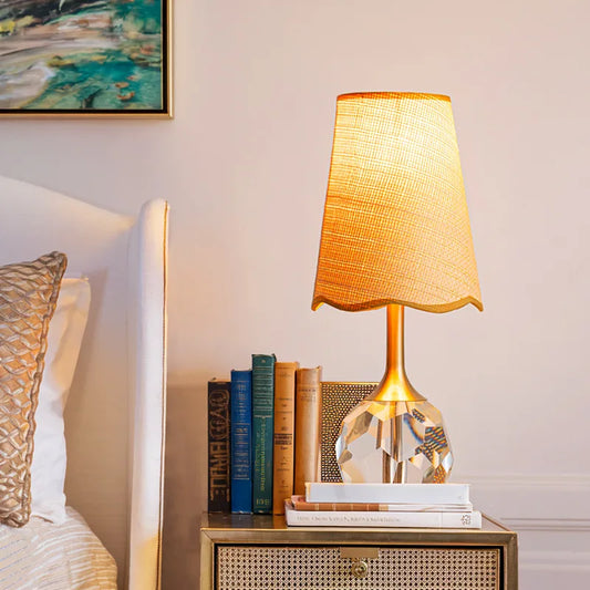 A gold and crystal table lamp on a nightstand next to books and a bed.