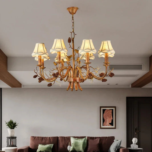 A gilded chandelier with intricate floral and bird details, illuminated in a modern living room above a sofa.