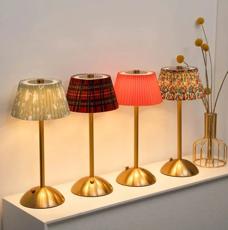 Four table lamps with different colored lampshades on a white surface.