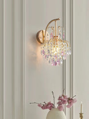 Gold wall sconce with cascading pink and clear teardrop crystals, mounted on a white paneled wall.