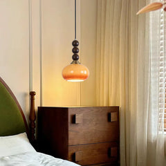 A single wood bead and persimmon-shaped globe pendant light hanging above a wooden dresser in a bedroom setting.