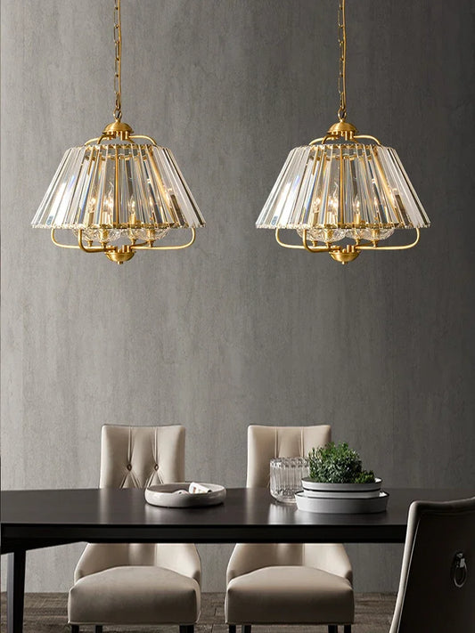 Two gold crystal faceted pendant lights hanging above a dining table with beige chairs.
