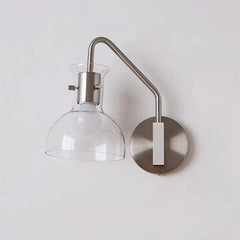 Brushed nickel wall sconce with a clear glass dome shade and an adjustable arm against a white wall.