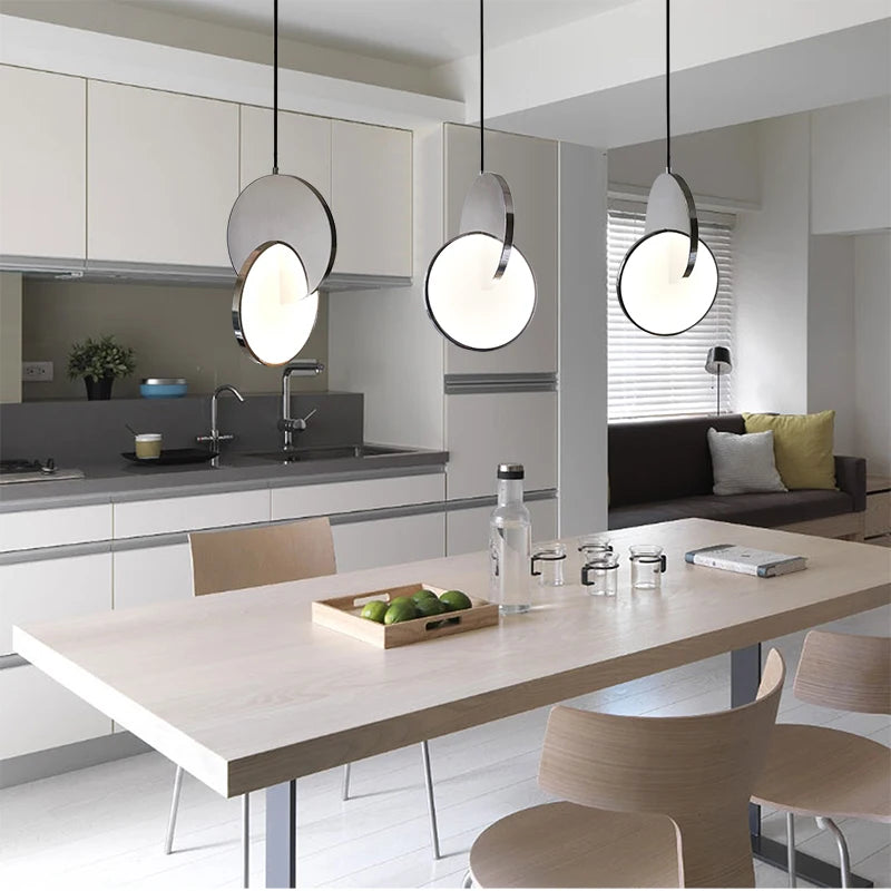 Polished steel geometric pendant lights above a dining table.