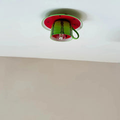 A whimsical green watermelon and coffee cup shaped ceiling light fixture mounted on a white ceiling, casting a soft shadow.