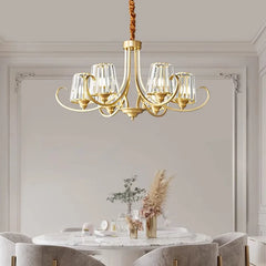 A polished gold chandelier with crystal elements is showcased above a dining table with upholstered chairs.