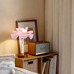 A white and pink petal-shaped table lamp placed on a shelf next to a framed picture and a vintage-style speaker.