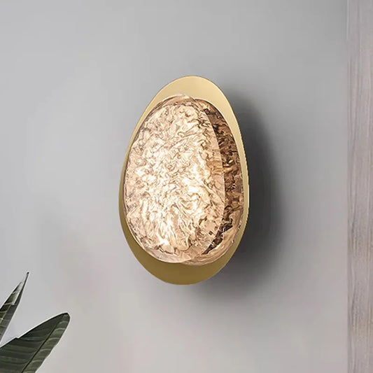 Gold textured resin egg-shaped wall sconce mounted on a light gray wall, showing its depth and shadow.