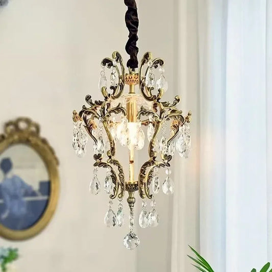 A gold crystal chandelier hanging against a white wall, showcasing its intricate design and crystal droplets.